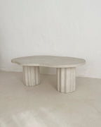 Table basse HESTIA ronde, plateau clair texturé et quatre pieds cylindriques cannelés.