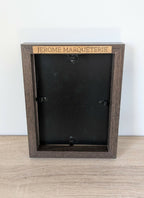Dos de tableau en bois foncé avec inscription « JEROME MARQUETERIE » et fixations