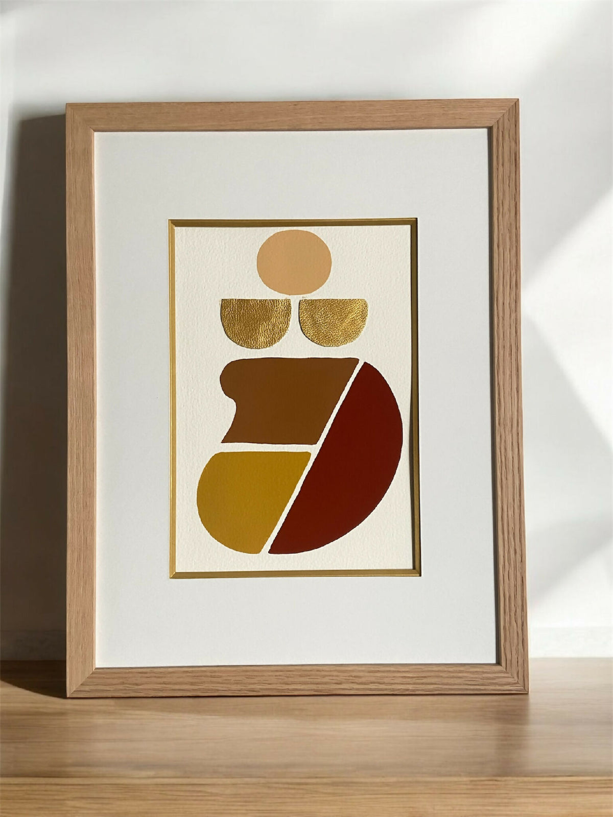 Tableau abstrait encadré en bois clair, illustration dorée et rouge, vue en biais.