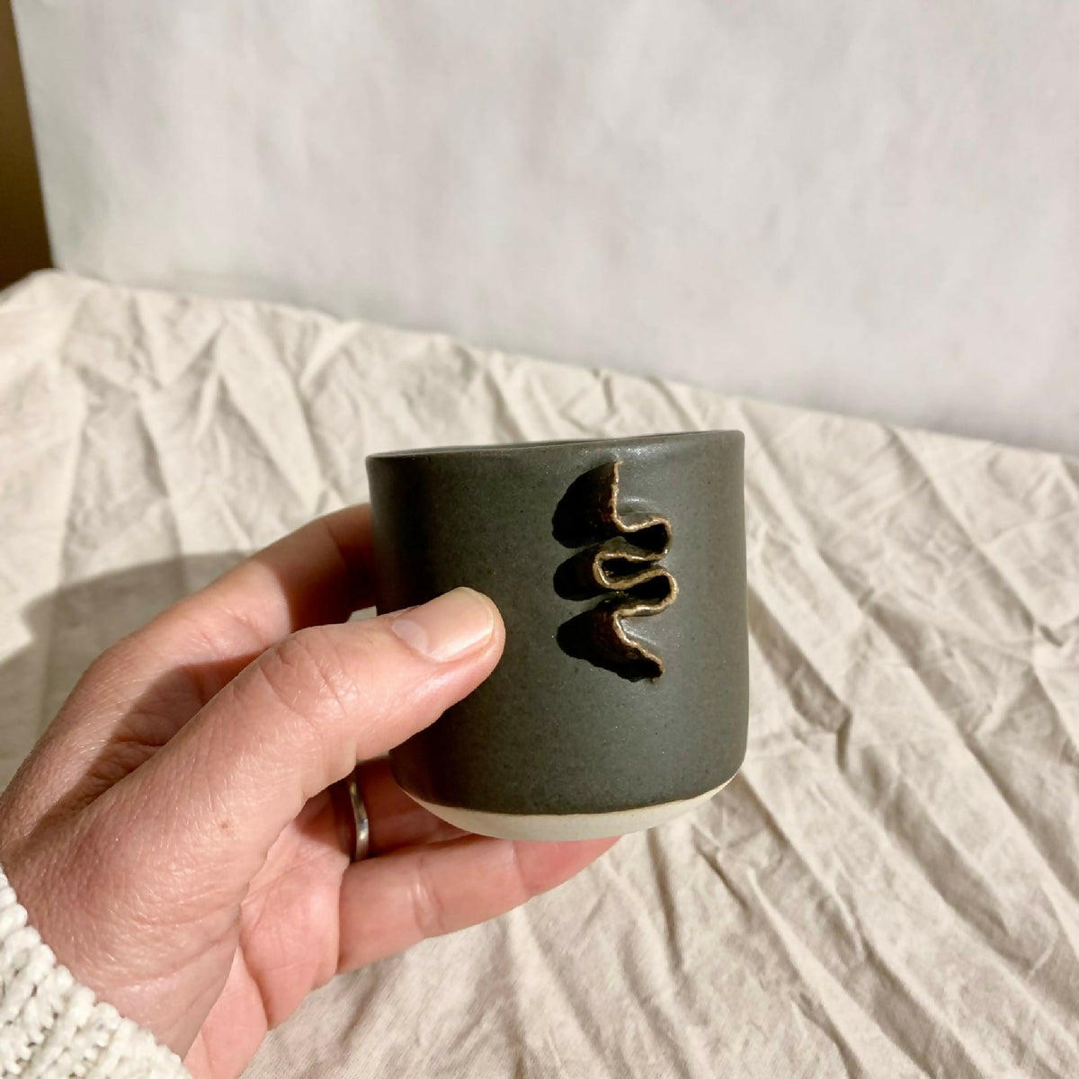 Tasse à café vert foncé, motif doré en relief, tenue en main.