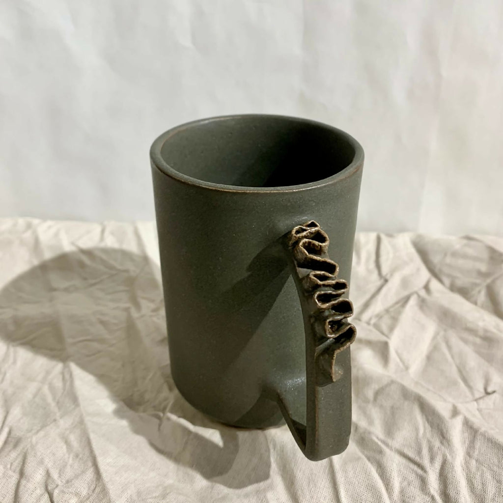 Tasse à thé kaki foncé en céramique, intérieur foncé et anse sculptée.