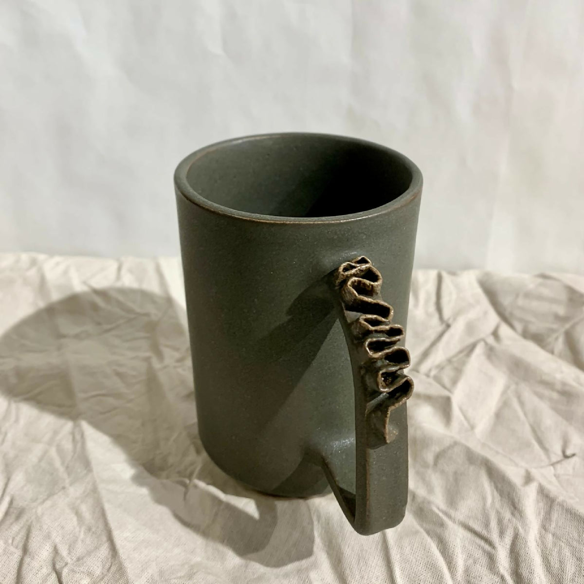 Tasse à thé kaki foncé en céramique, intérieur foncé et anse sculptée.