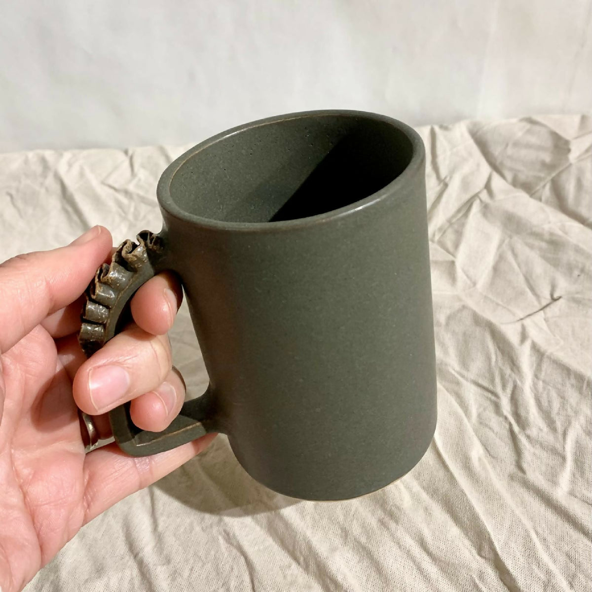 Tasse à thé kaki foncé en céramique, vue de côté avec anse sculptée.