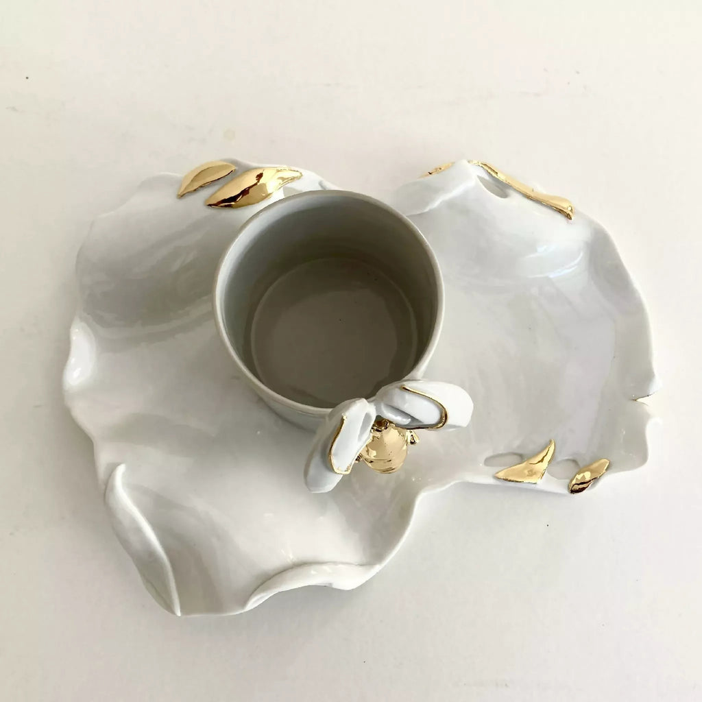 Tasse blanche posée sur soucoupe homard ronde, motif et finitions dorées.