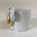 Tasse blanche avec figurine de homard doré accrochée à l’anse