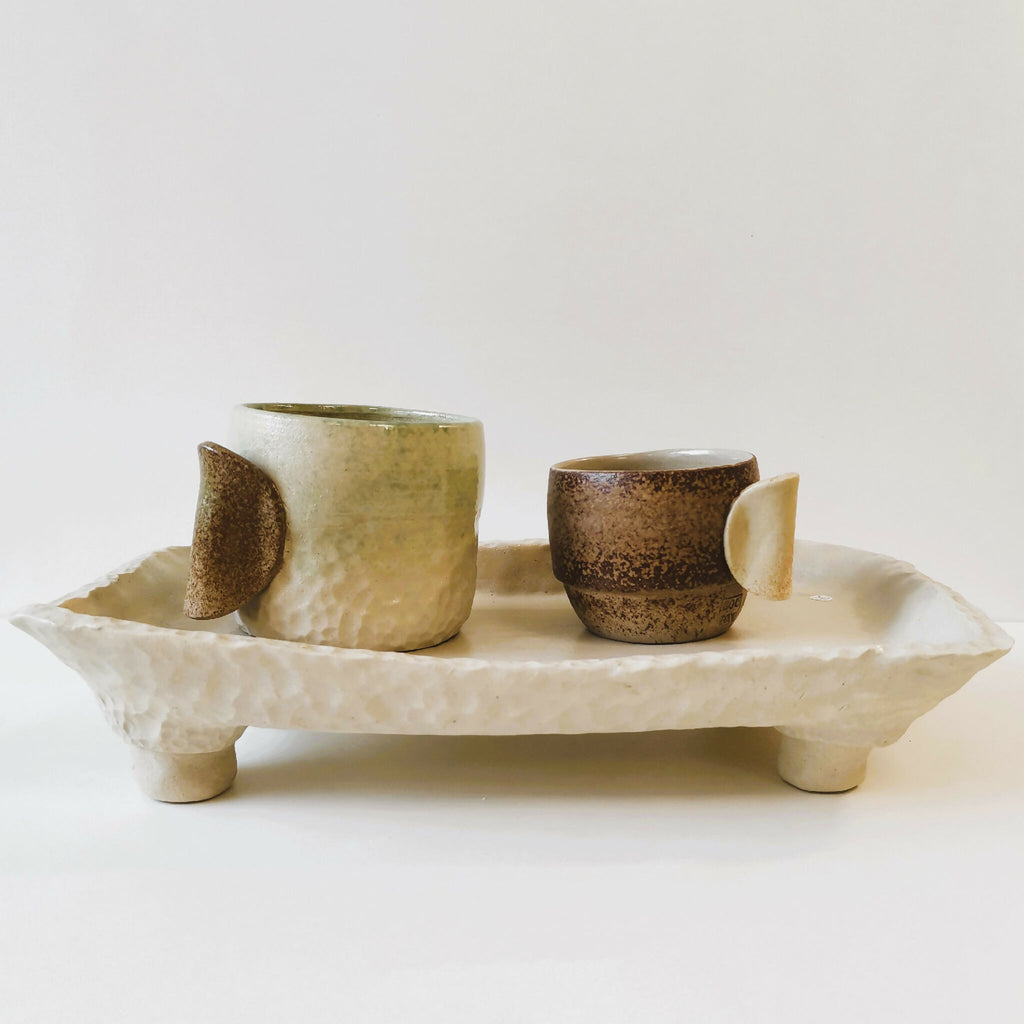 Tasses en céramique sur plateau sculpté, une tasse marron et deux vertes