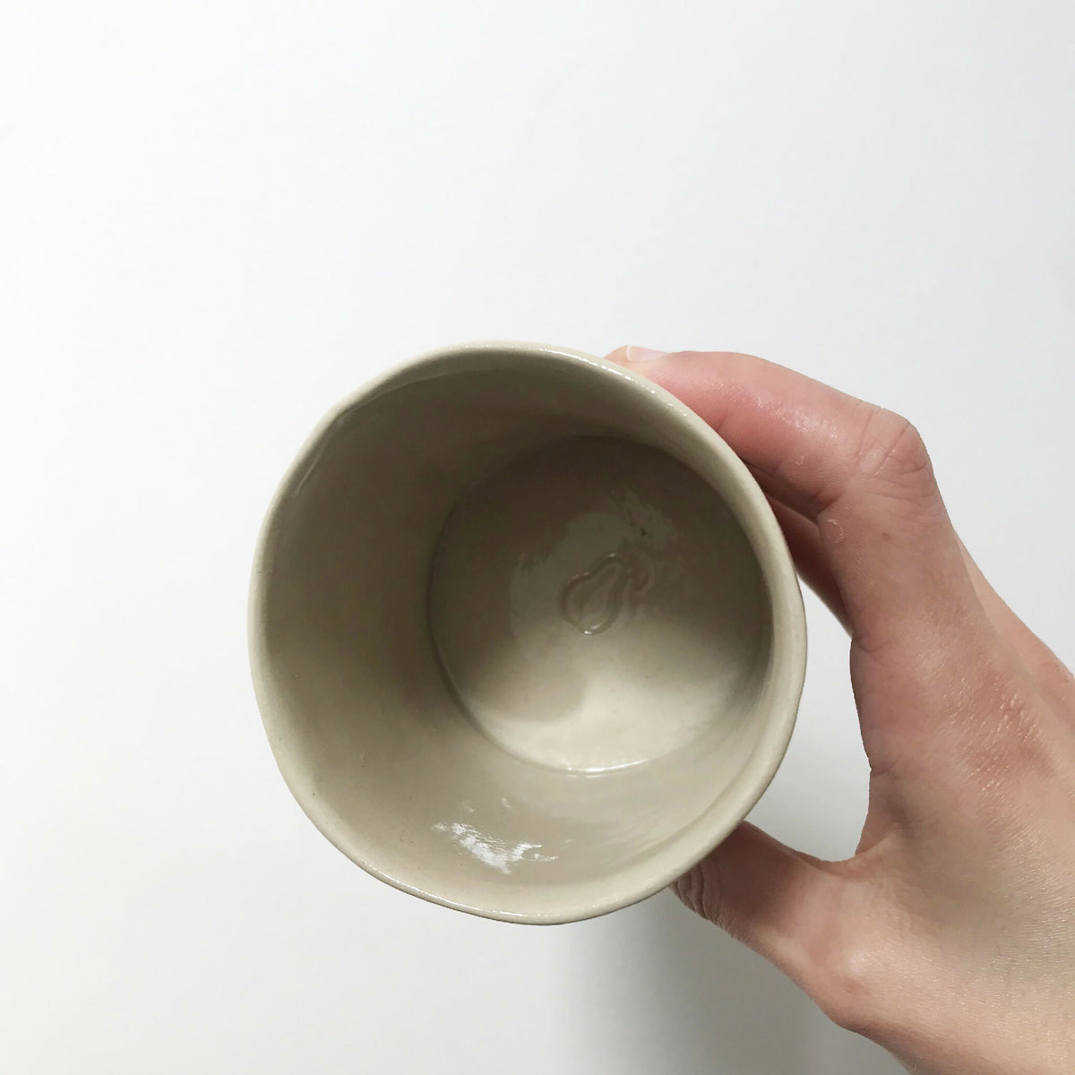 Tasse en céramique beige, vue intérieure, tenue par une main