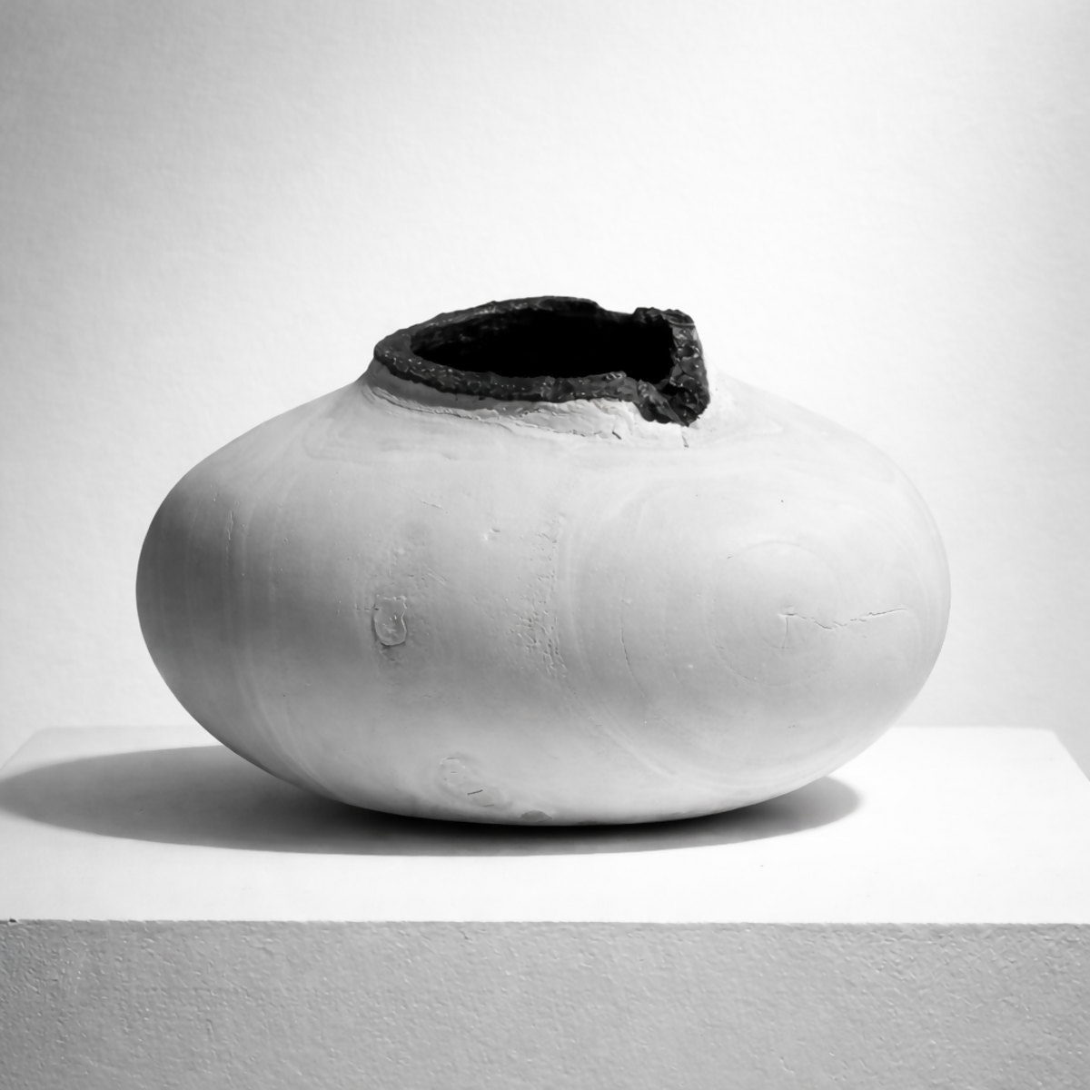 Vase céramique blanche à ouverture sombre sur le dessus, forme arrondie.