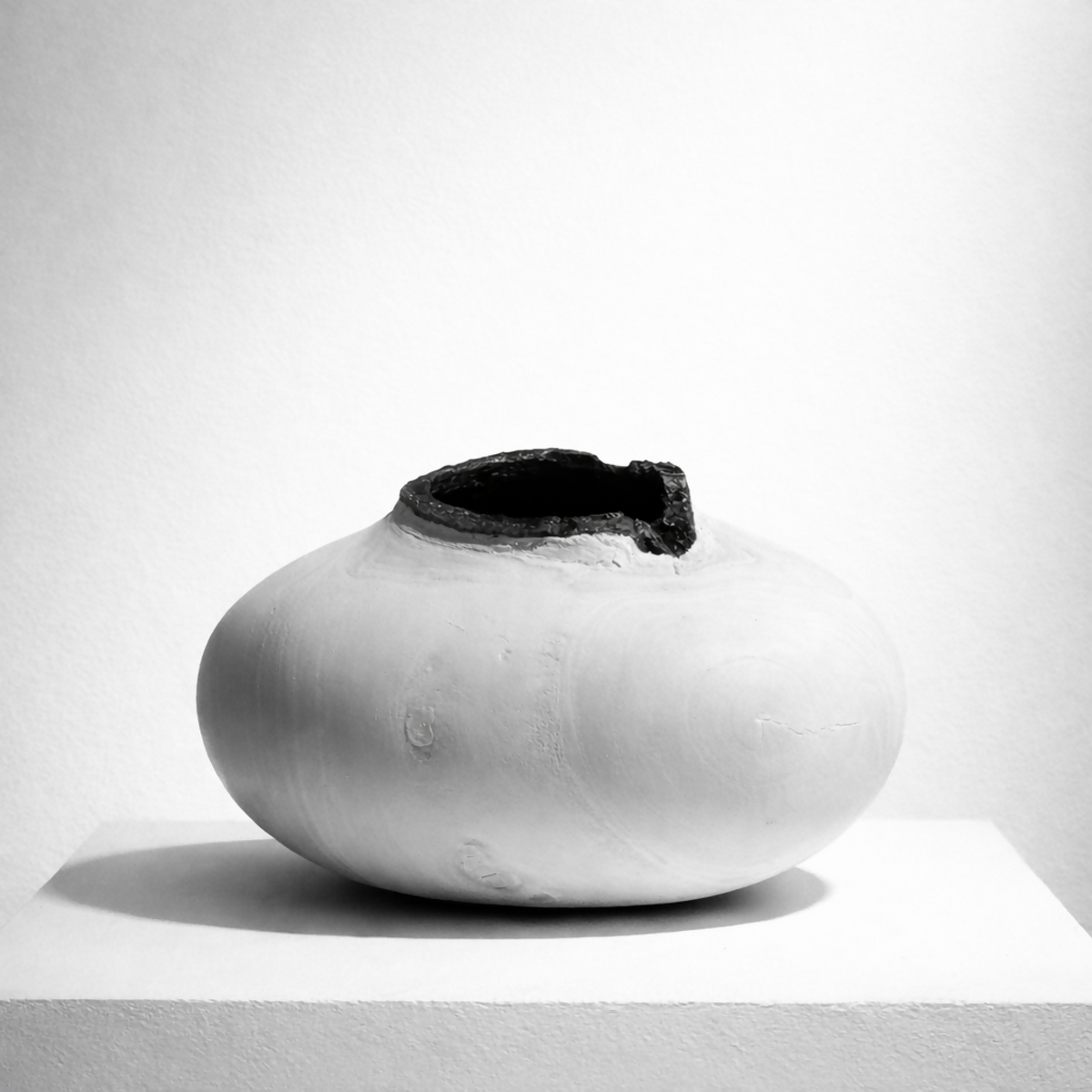 Vase céramique blanche ronde avec ouverture sombre au centre, silhouette épurée.