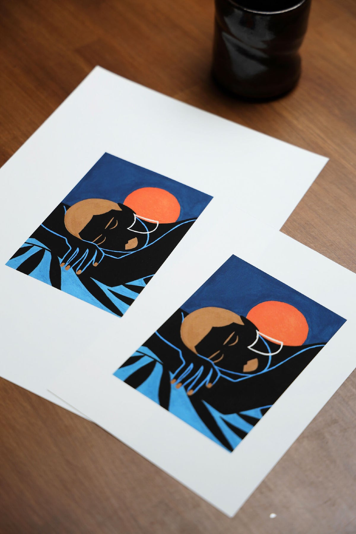 Deux cartes imprimées sur papier blanc avec personnage noir, soleil orange et fond bleu