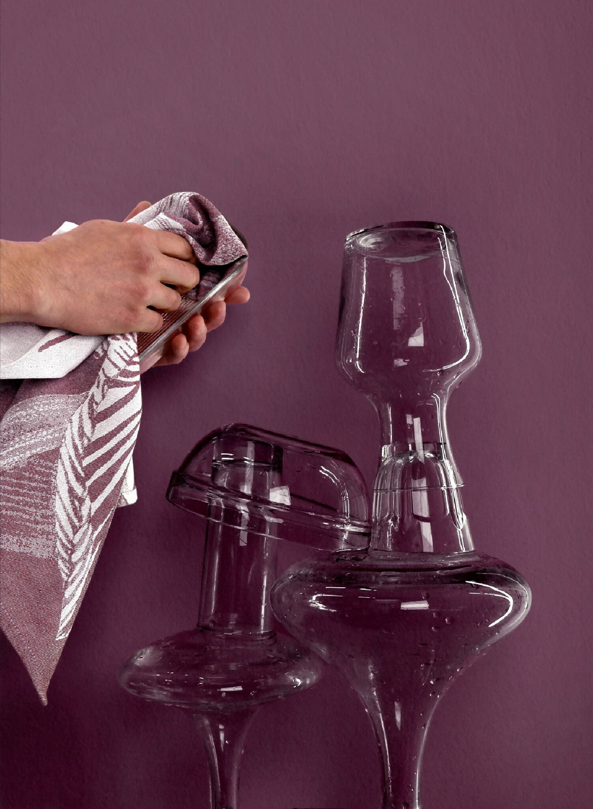Torchon imprimé tenu par une main, motif plumes violet près de verres.