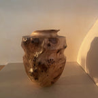 Vase artisanal en bois sculpté, forme organique, veines et taches foncées.