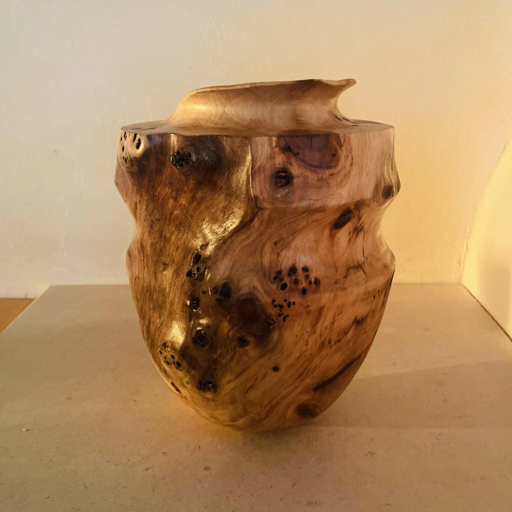 Vase en bois sculpté, vue de trois-quarts, ouverture ronde, bord évasé et taches.