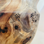 Détail du vase en bois : zones brun clair, nœuds et taches foncées, veinage.