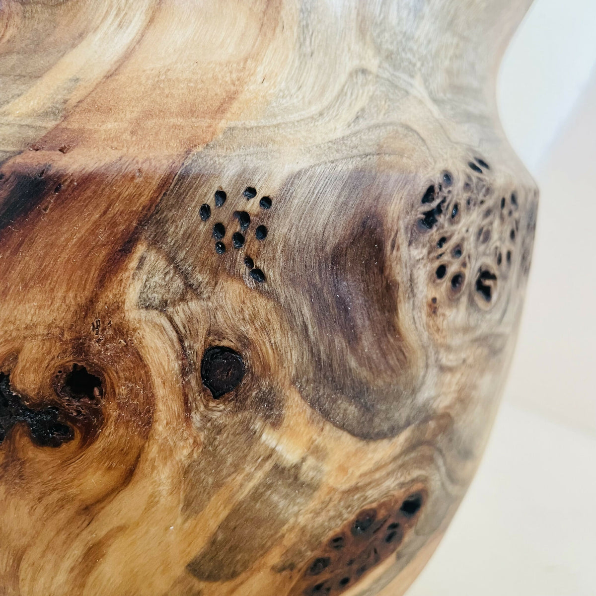 Détail du vase en bois : zones brun clair, nœuds et taches foncées, veinage.