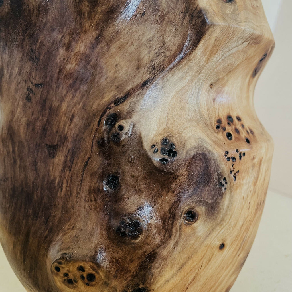 Détail du vase en bois sculpté : nœuds noirs, taches ponctuelles, veines torsadées.