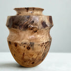 Vase en bois sculpté, tons miel et bruns, incrustations sombres, contours irréguliers.