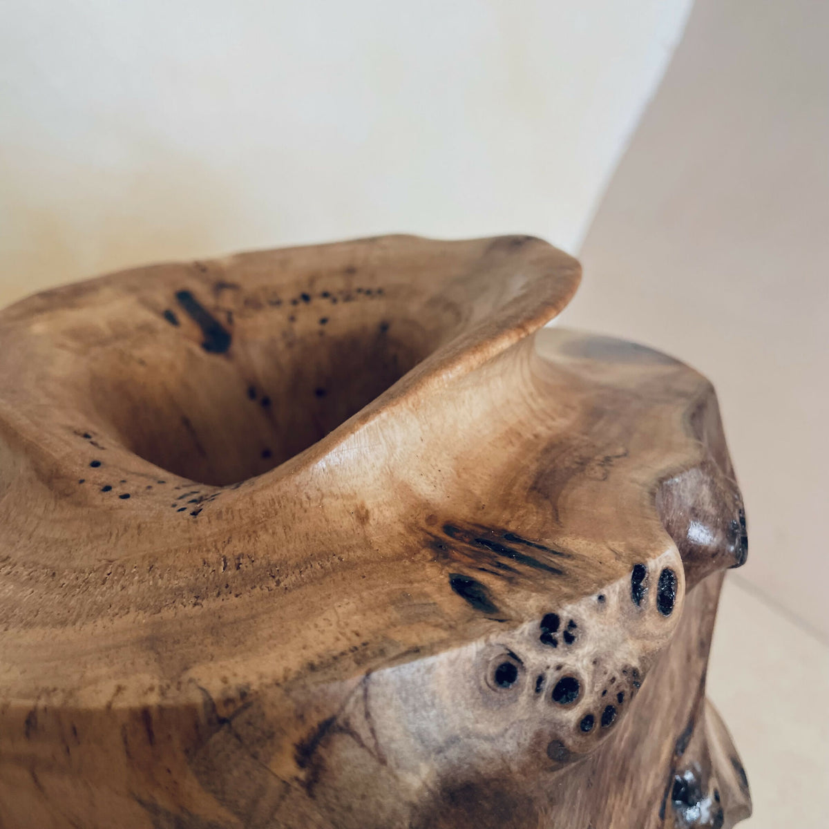 Vue rapprochée : vase en bois sculpté, intérieur creux et motif sombre sur la paroi.