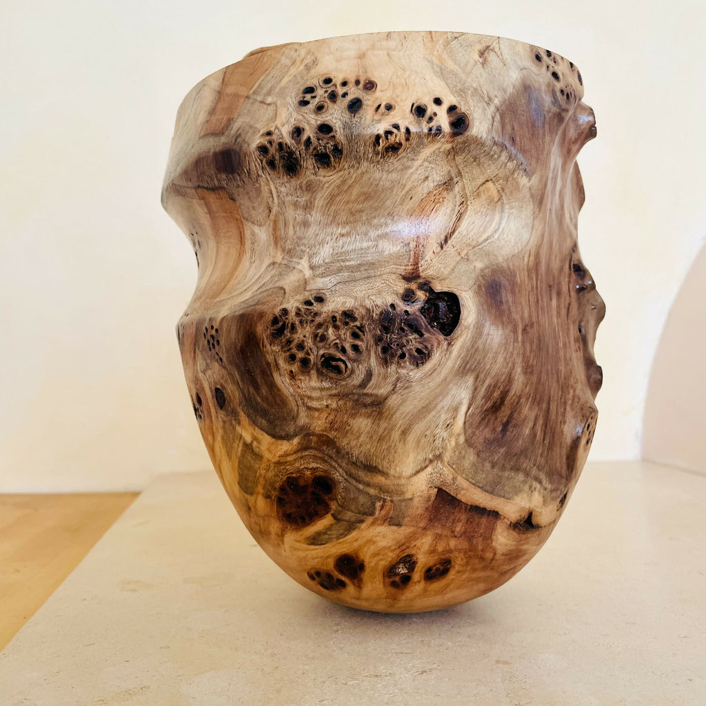 Vase en bois sculpté, couleur claire, taches et points sombres, silhouette arrondie.