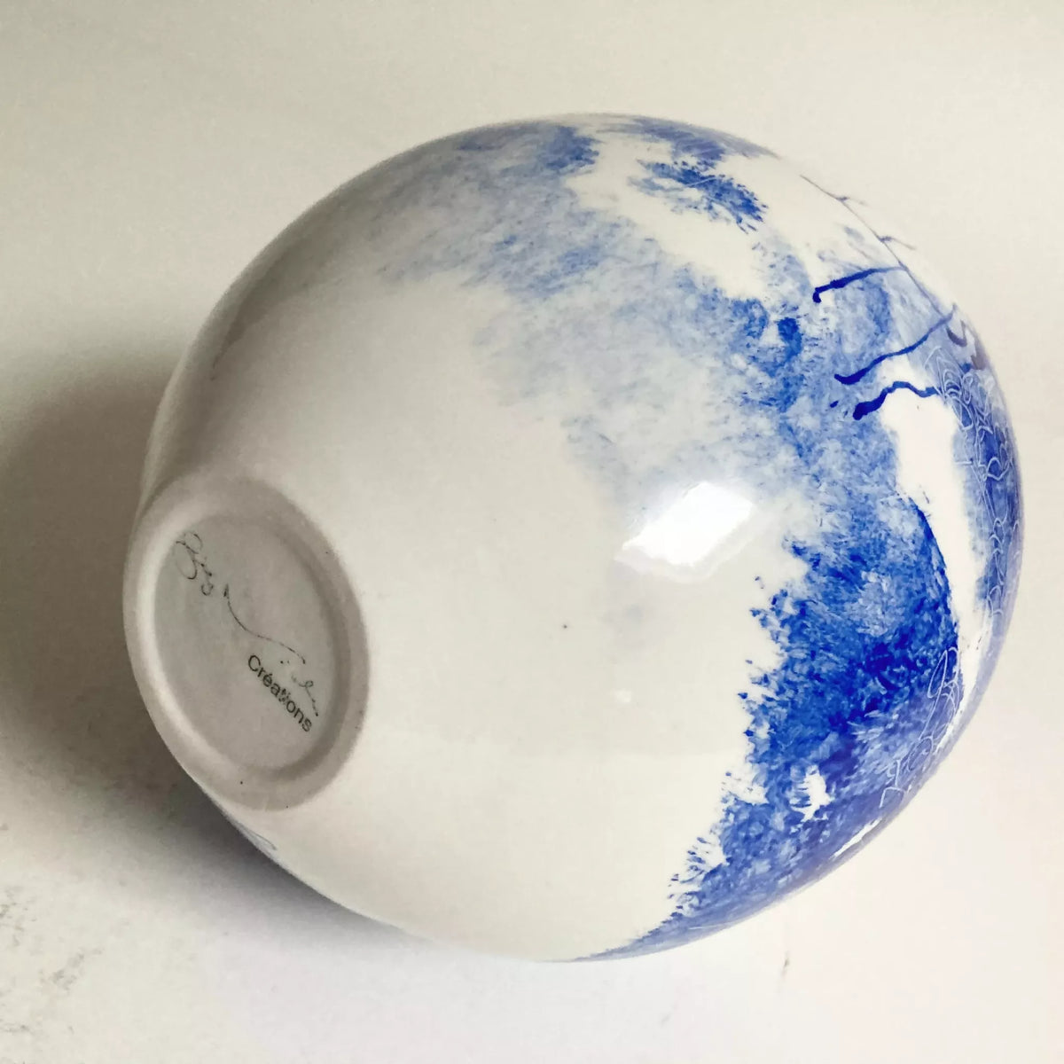 Base de vase blanc à bord bleu, dessous circulaire et logo en relief.