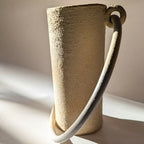 Vase en céramique beige à anse courbée, gros plan sur la texture.