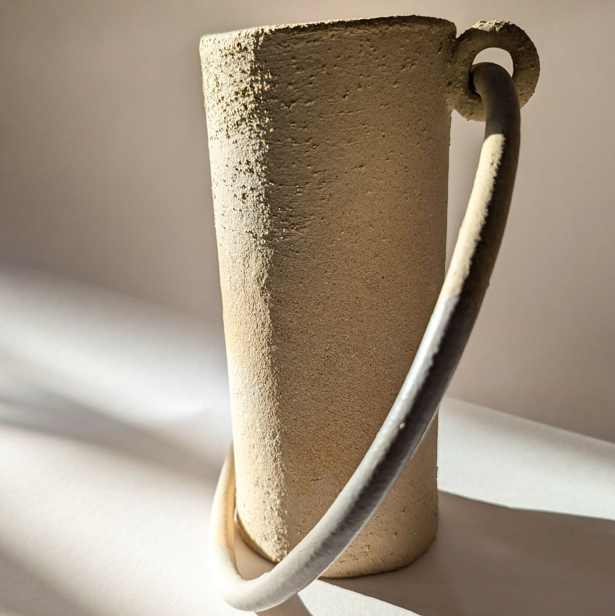 Vase en céramique beige à anse courbée, gros plan sur la texture.