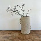 Vase en grès beige piqueté avec reliefs ronds sur le côté, silhouette cylindrique.
