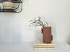 Vase en grès brun avec bouquet de fleurs violettes, posé sur des livres.