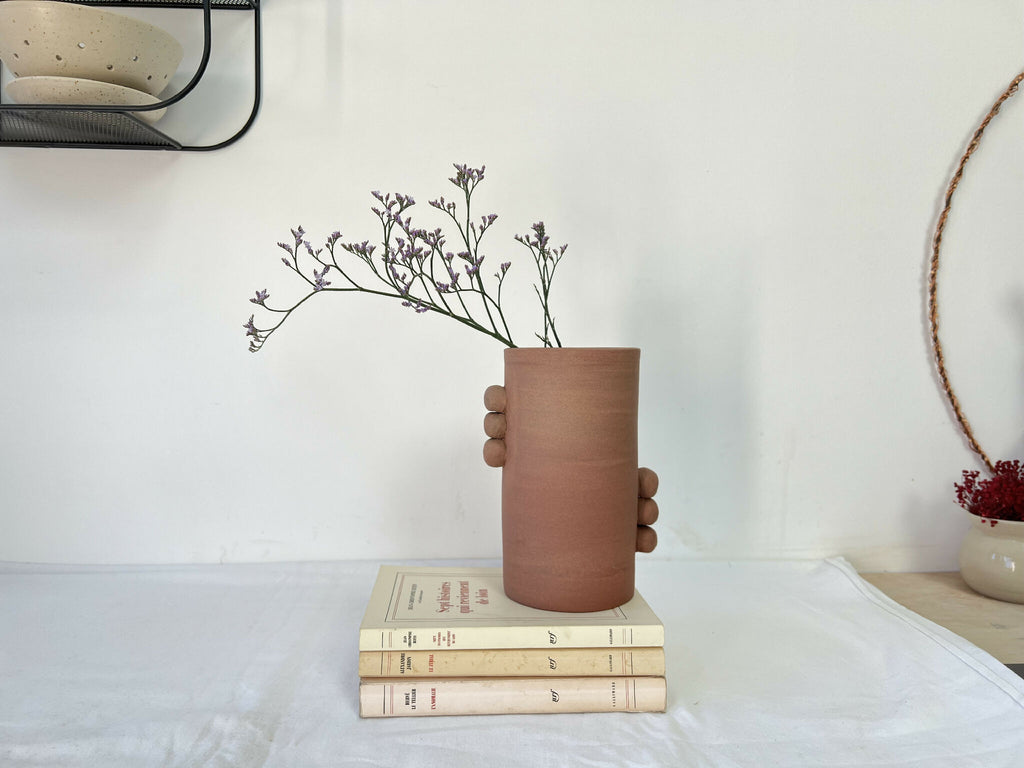 Vase en grès brun cylindrique à poignées, bouquet violet posé sur des livres.