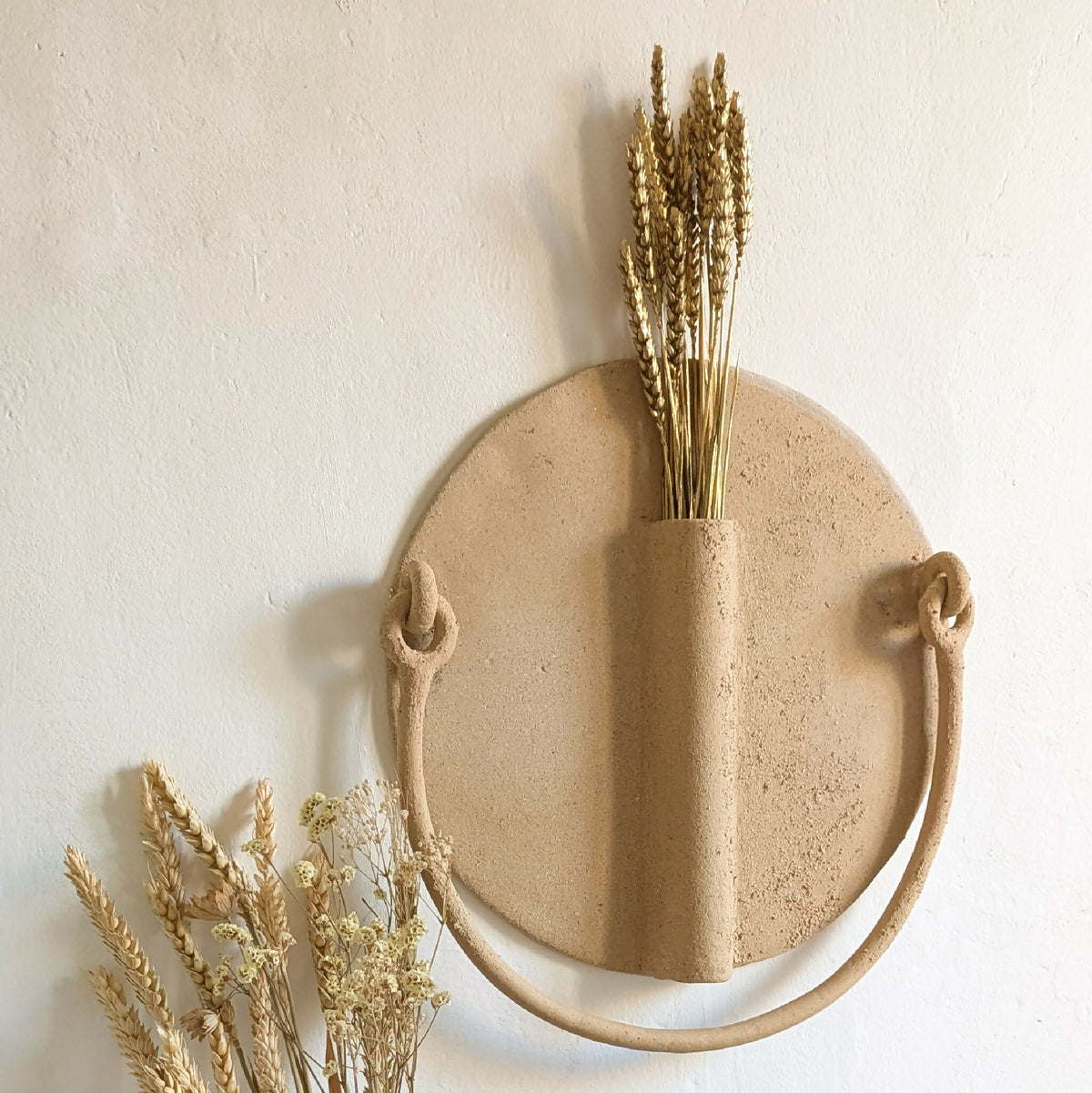Vase mural en céramique beige façon soleil, anse ronde et ouverture pour tiges