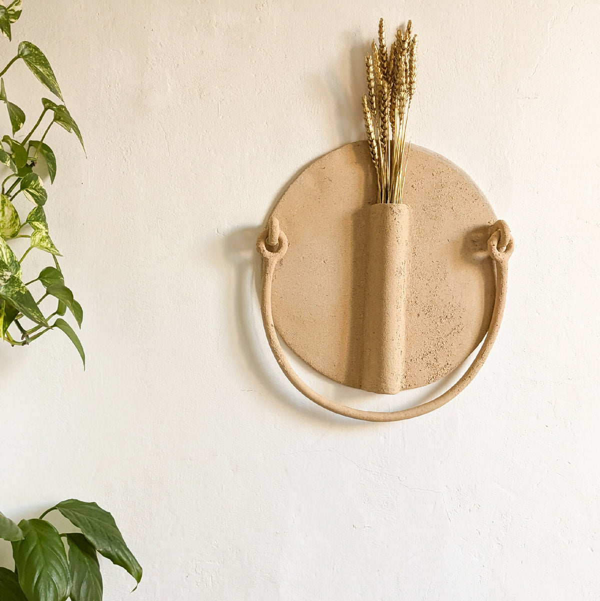 Vase mural en céramique beige en forme de soleil avec ouverture et anse, fixé au mur