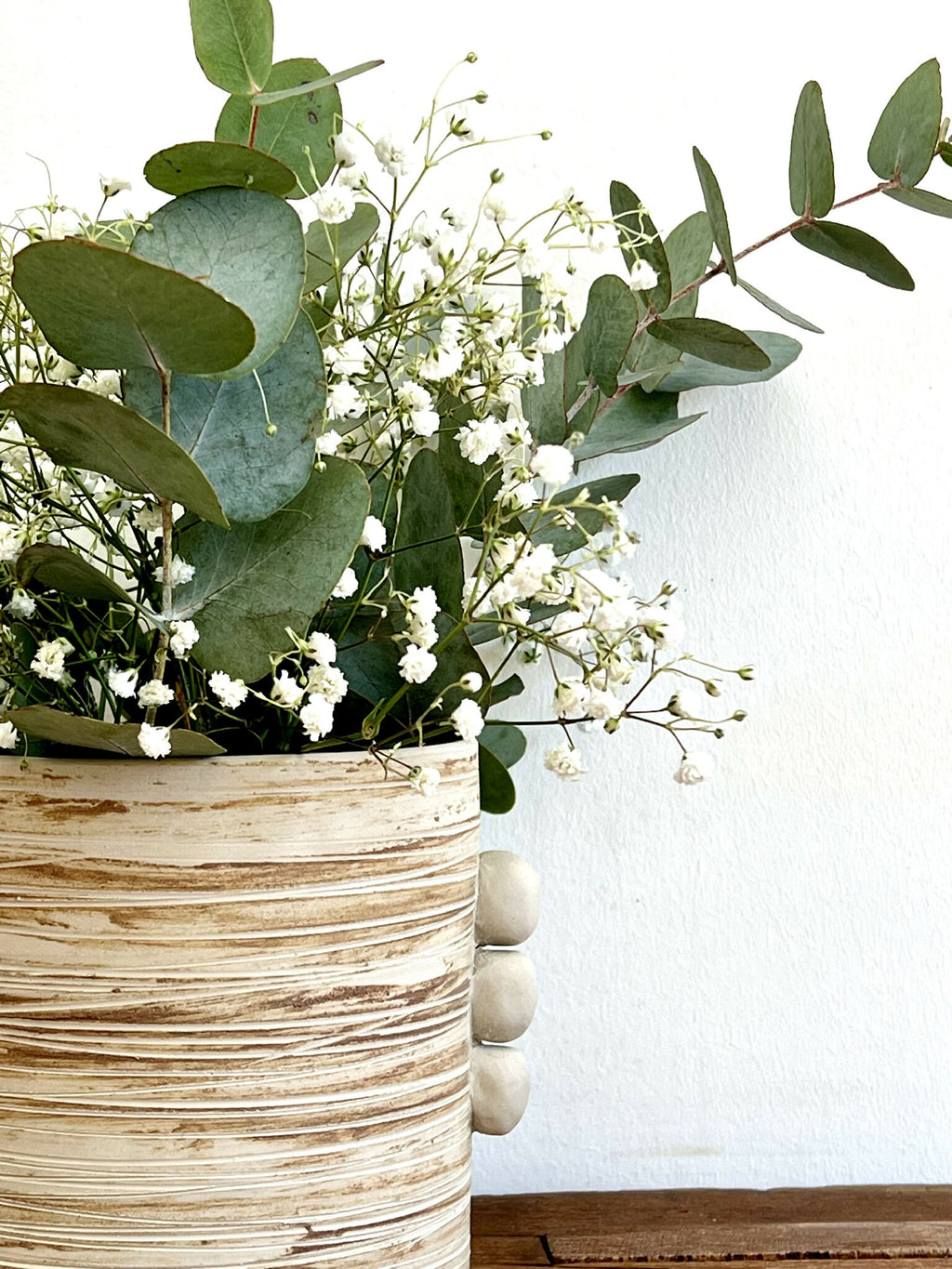 Vase cylindrique grès marbré beige, bord côtelé, renflements, bouquet de fleurs blanches.