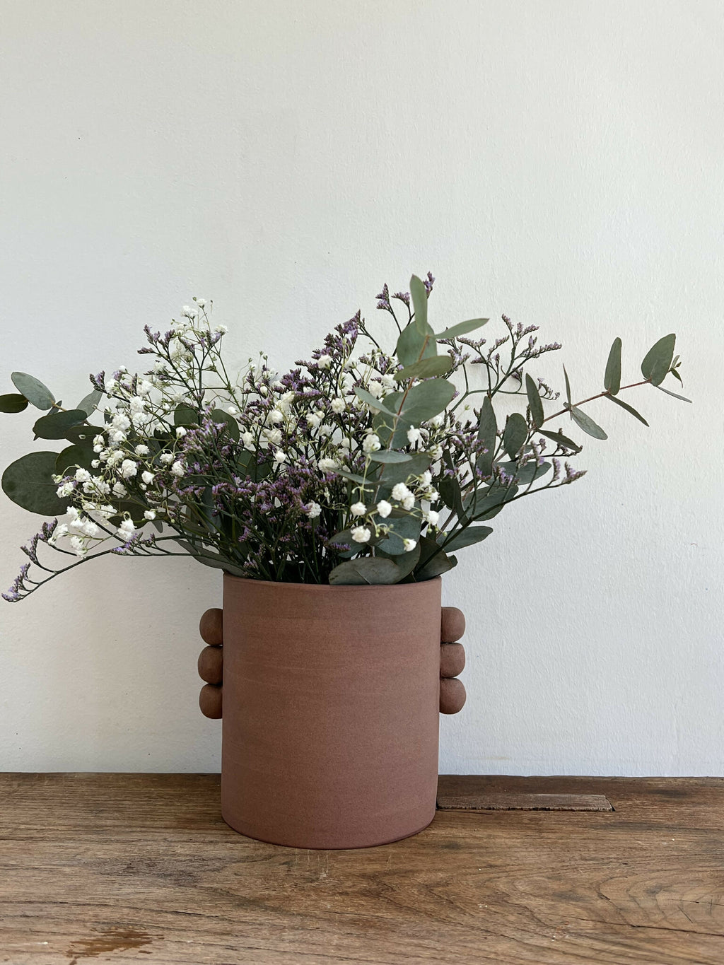 Vase en grès roux PALMA, bouquet de fleurs blanches et mauves, tiges et feuilles visibles.