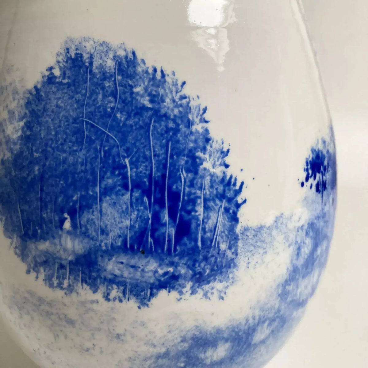 Vase en céramique goutte blanche, détail du paysage bleu à la surface.