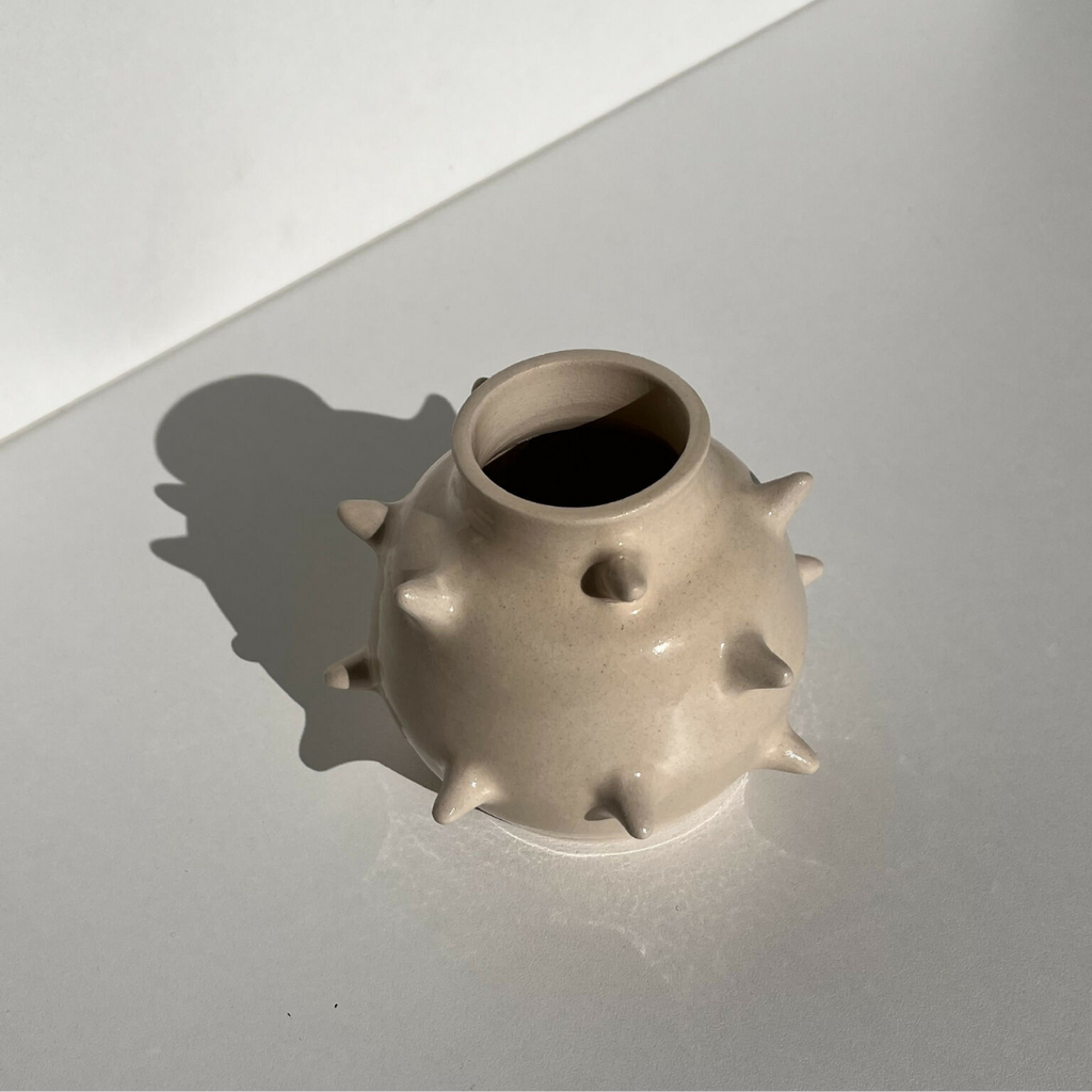 Vase en céramique beige à piques autour du bord, ouverture supérieure noire.