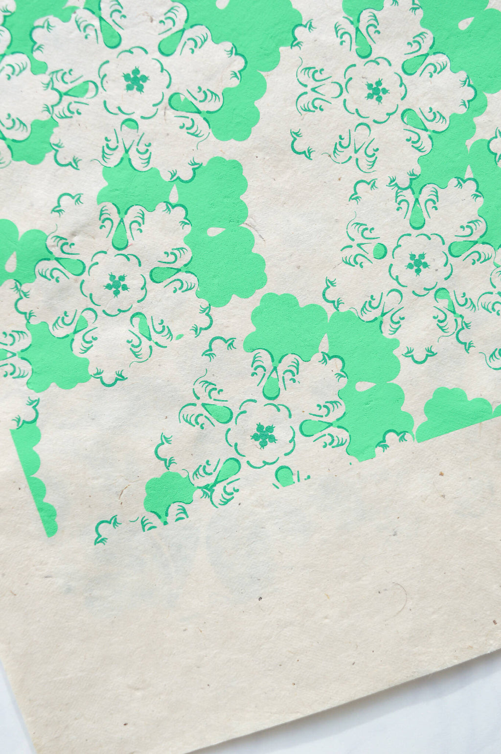 Papier décoratif vert et blanc à motifs floraux, bord en diagonale.